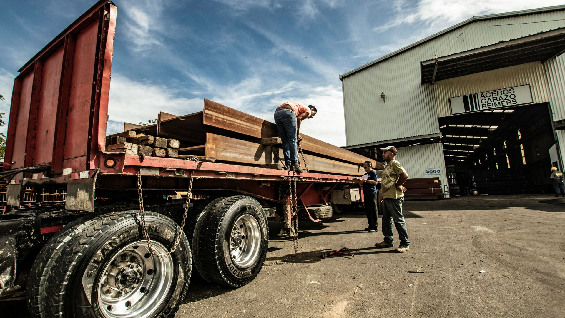 Workers loading lumber onto a flatbed truck at an industrial yard