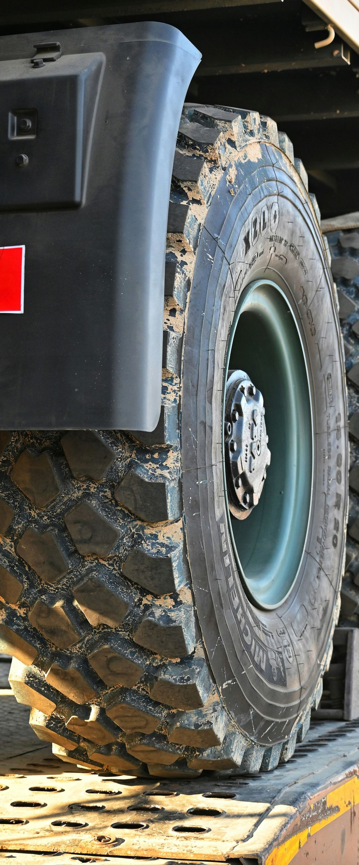 Close-up of a black off-road tire with deep treads on a vehicle, resting on a metal ramp.