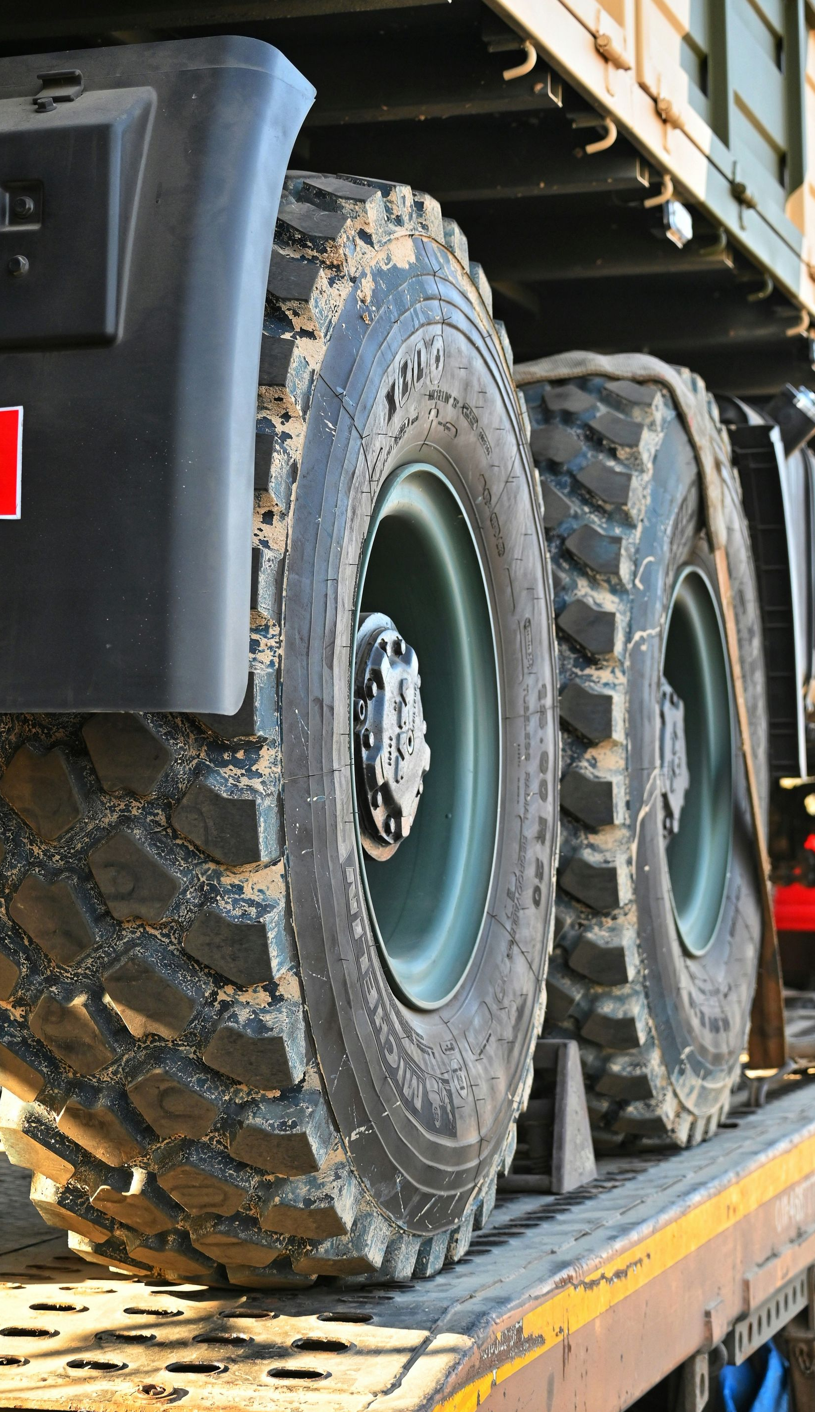 Close-up of two large, deep-tread military truck tires mounted on olive-drab rims, resting on a flatbed transport vehicle.