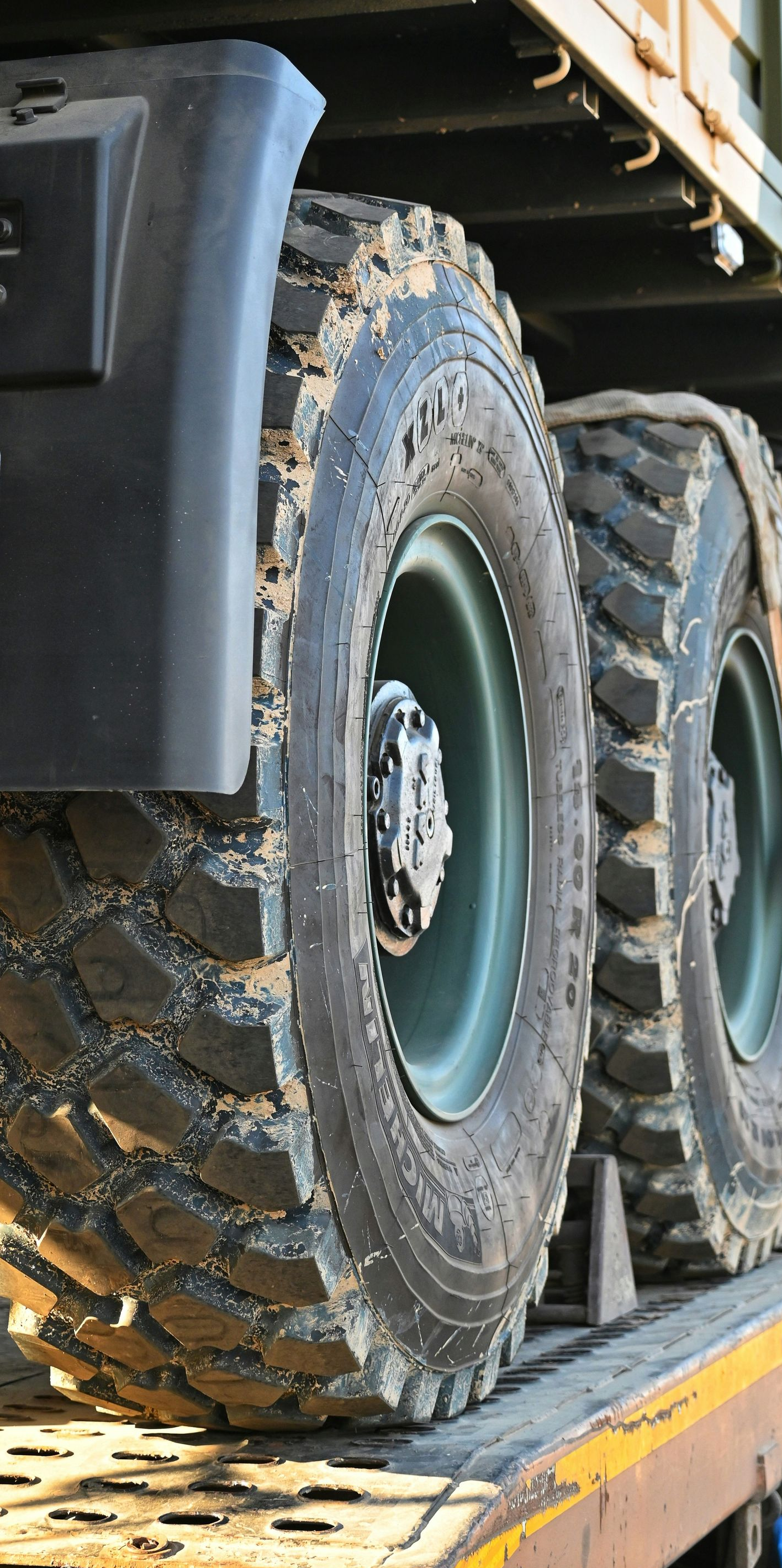 Close-up of a military truck’s large muddy tires on a loading ramp