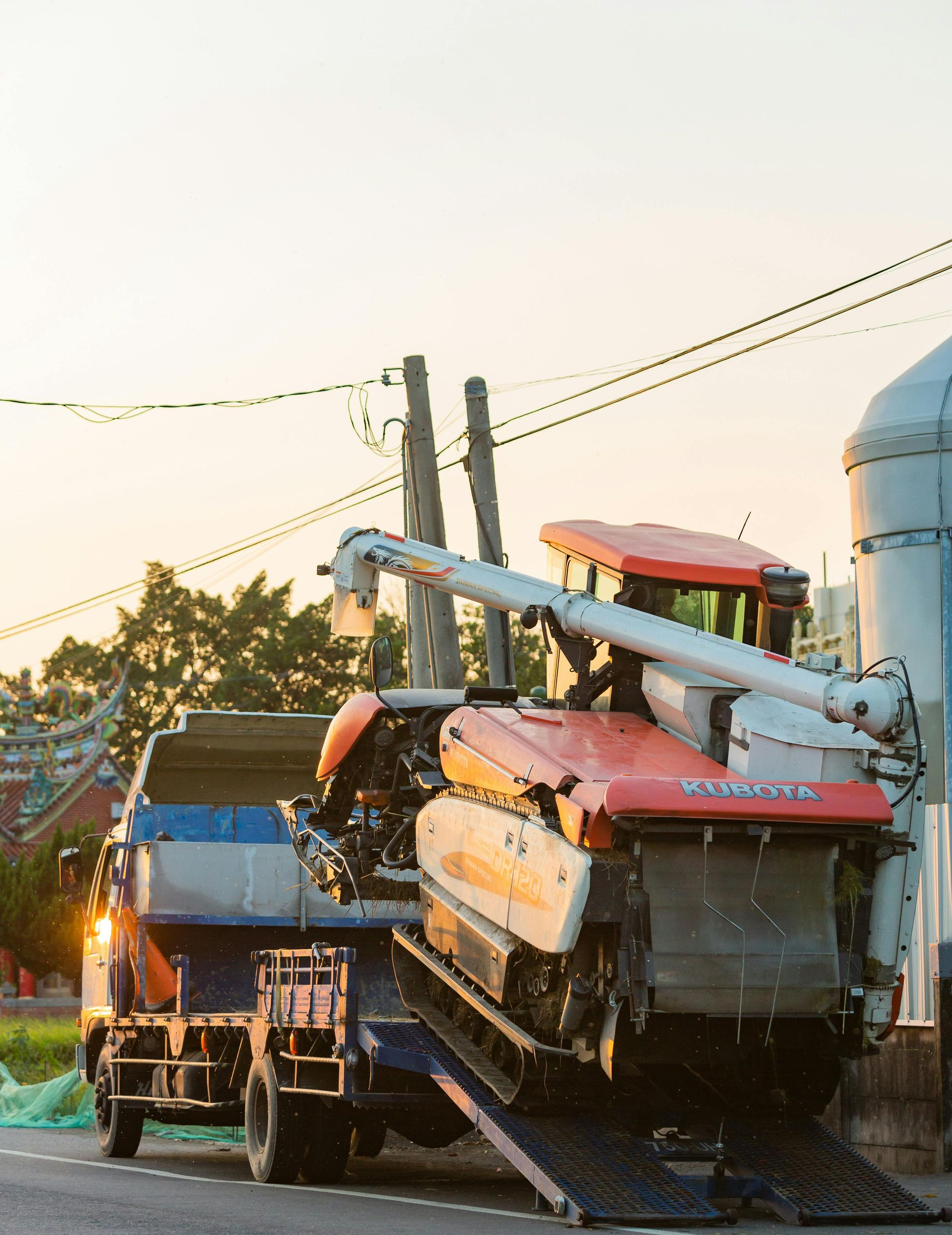 Overloaded farm machinery on a flatbed truck parked roadside at sunset