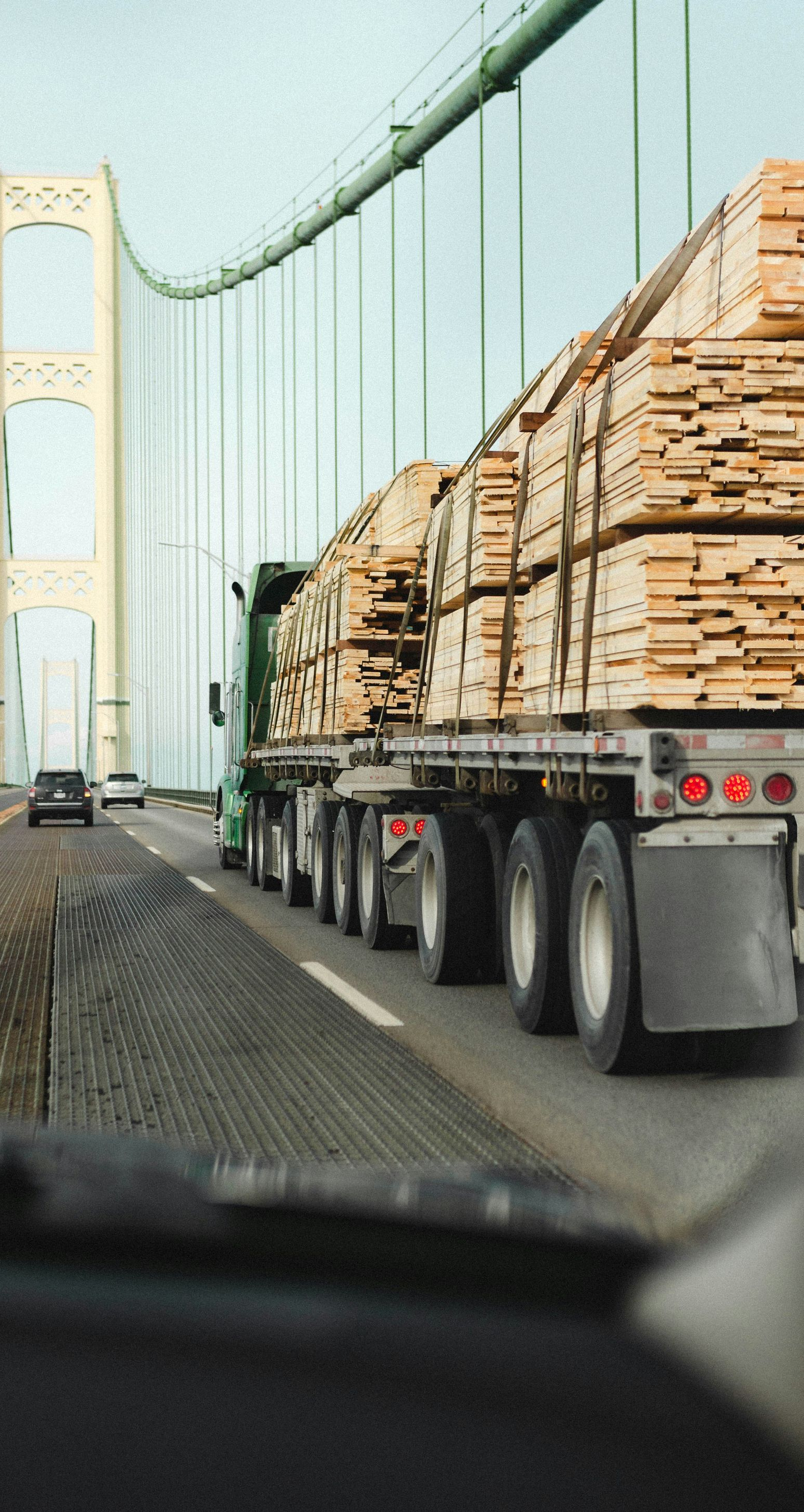 Flatbed truck loaded with lumber driving on a suspension bridge in light traffic