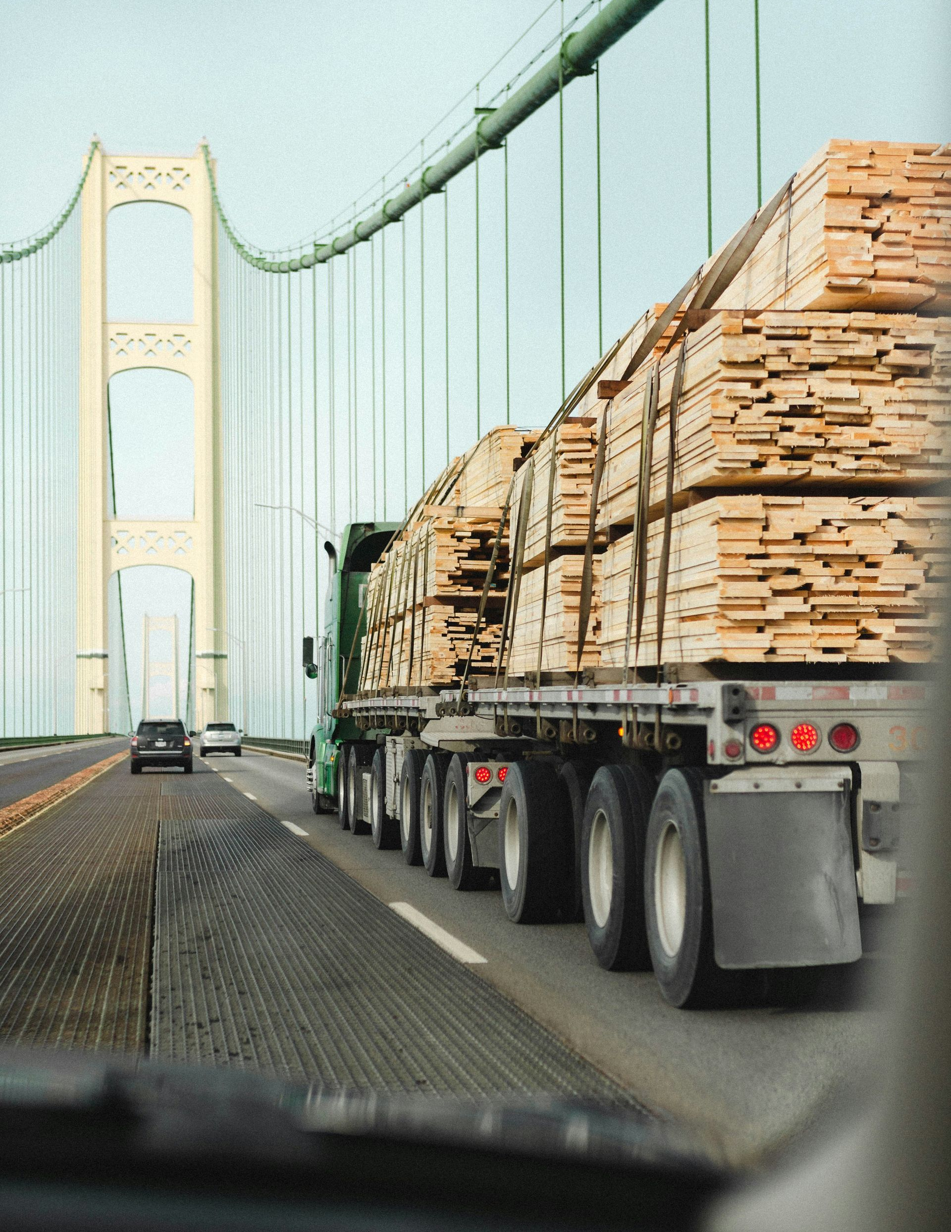 Logging truck driving on a suspension bridge over water, seen from inside another vehicle