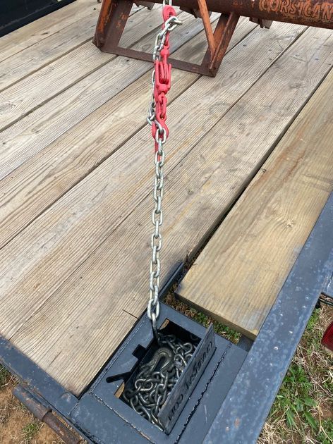 A chain suspended from a hook on a trailer. The chain leads down into a metal storage box filled with more chain.