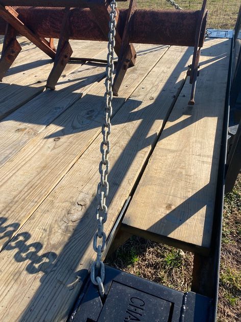 A metal chain hangs from a piece of equipment on a wooden trailer bed, casting a long shadow.