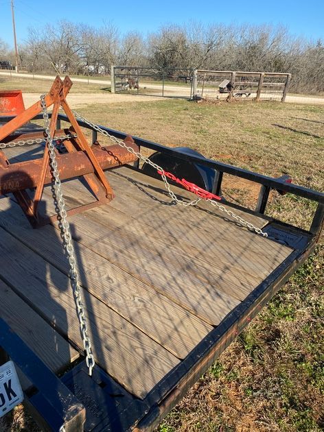 A rusted farm implement secured with chains on a wooden-floored trailer outdoors.