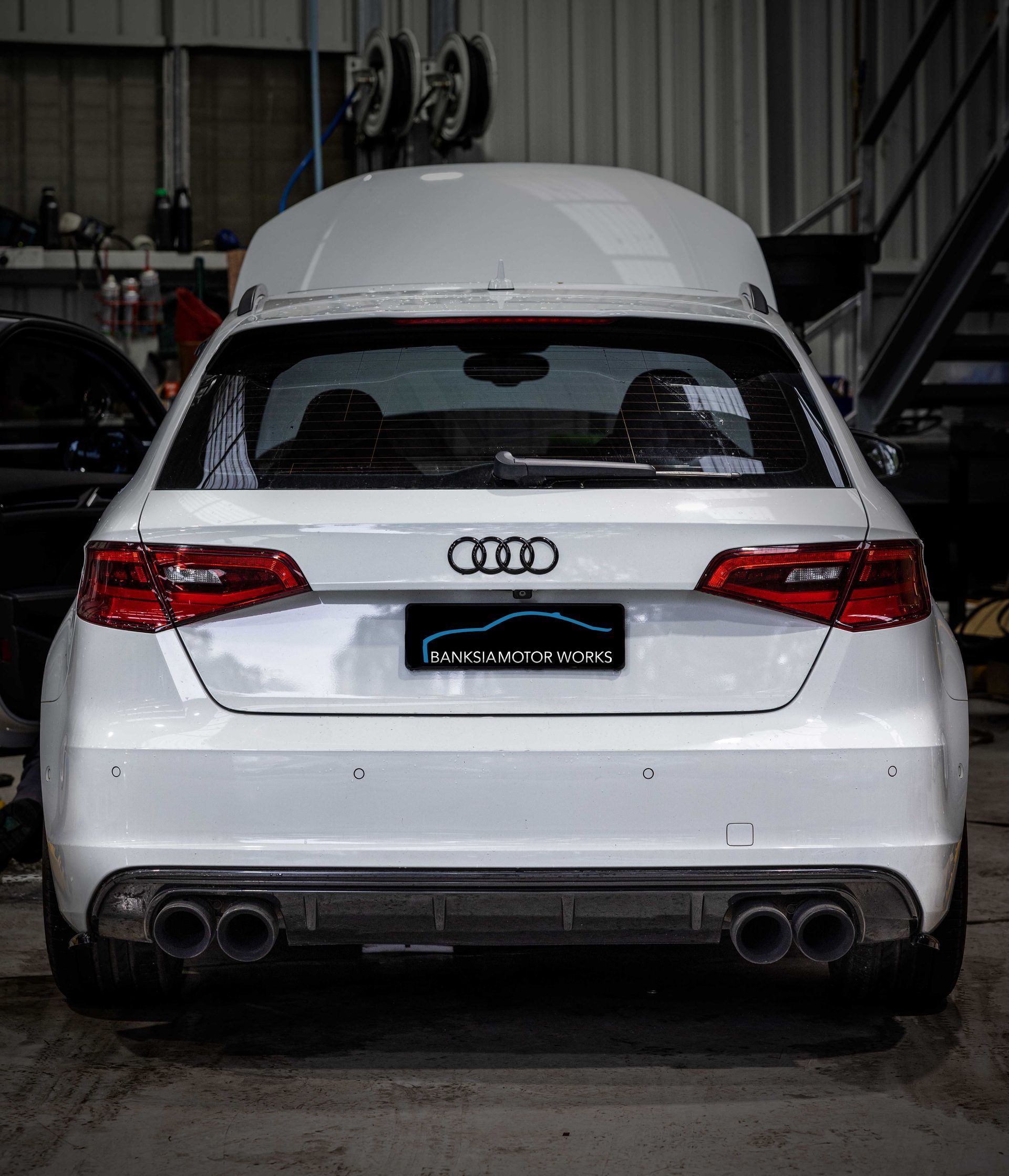 A white audi a3 is parked in a garage with the hood up.