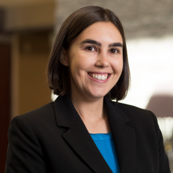 Studio portrait of a woman with a black blazer and blue blouse against an office background