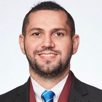 Headshot of a smiling man in a dark suit, white shirt, and blue tie on a white background