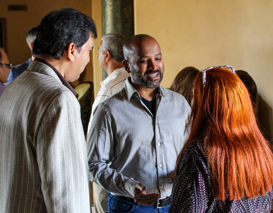 Three people chatting indoors, one man smiling at a woman with bright red hair.
