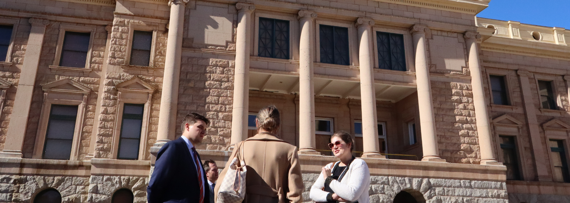 People walking in front of a grand stone building with tall columns and arches