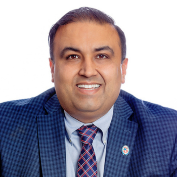 Professional headshot of a smiling person in a dark suit and tie against a light background
