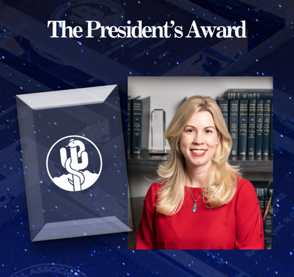 The President’s Award plaque beside a smiling blonde woman in a red top, with bookshelves behind her