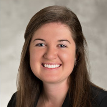 Studio headshot of a person in a blue blouse against a gray background