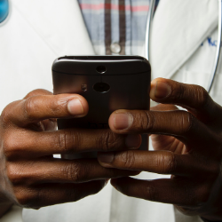 Hands holding a smartphone, thumbs poised over the screen, with a white shirt in the background