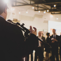 Person speaking at a microphone in a warmly lit indoor event with an audience in the background