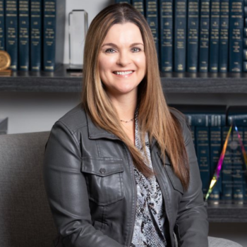 Smiling woman in a black jacket seated before a bookshelf in an office setting
