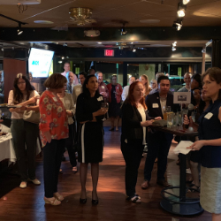 People mingling and holding drinks at a dimly lit indoor networking event.