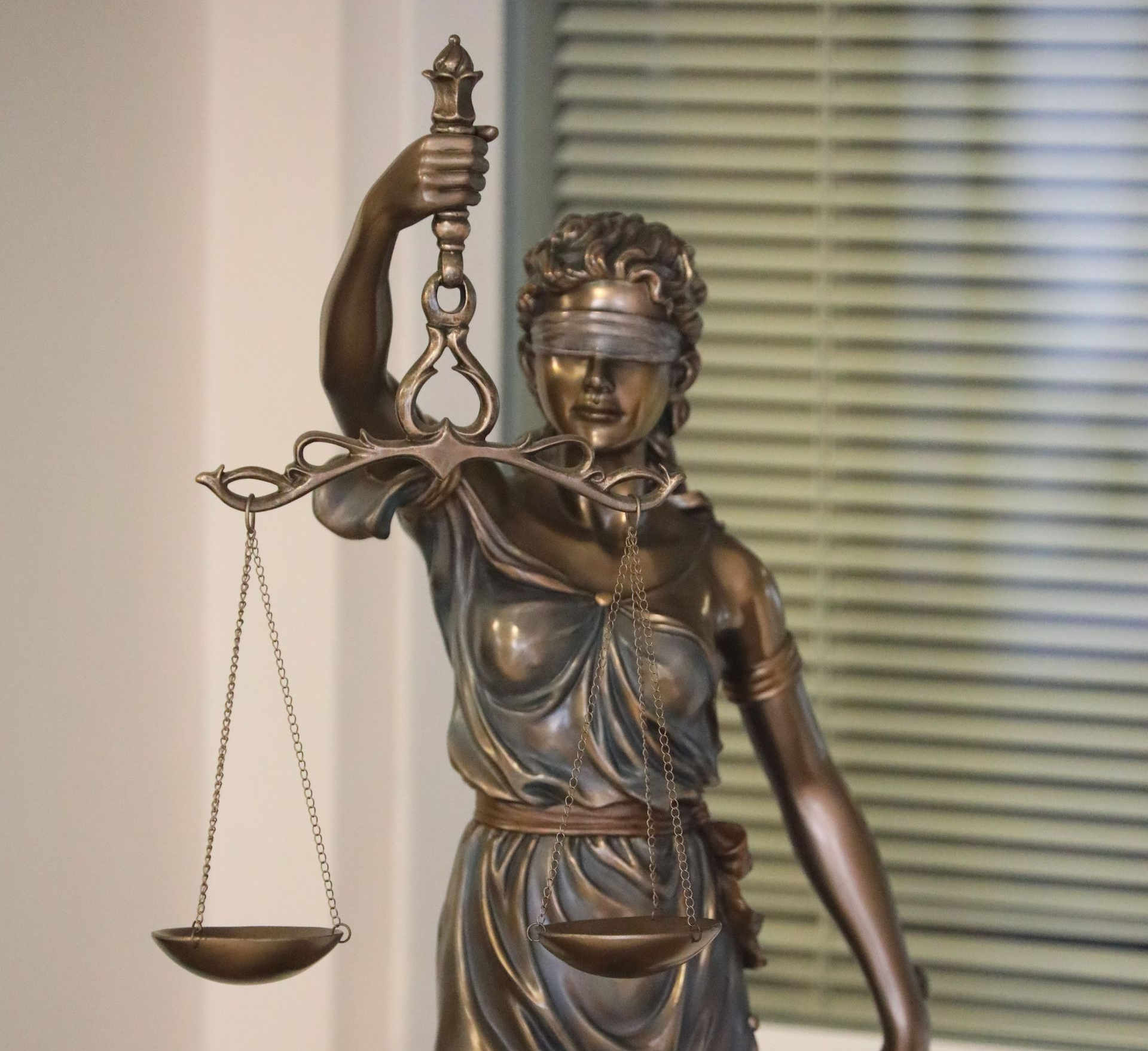 A statue depicting Lady Justice holding the scales of law stands outside of a building.