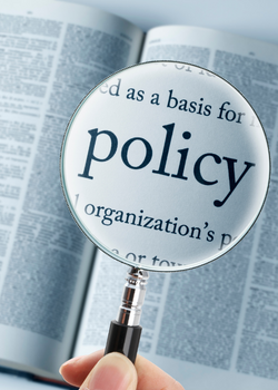 A magnifying glass hovers over the word 'policy' in a dictionary.