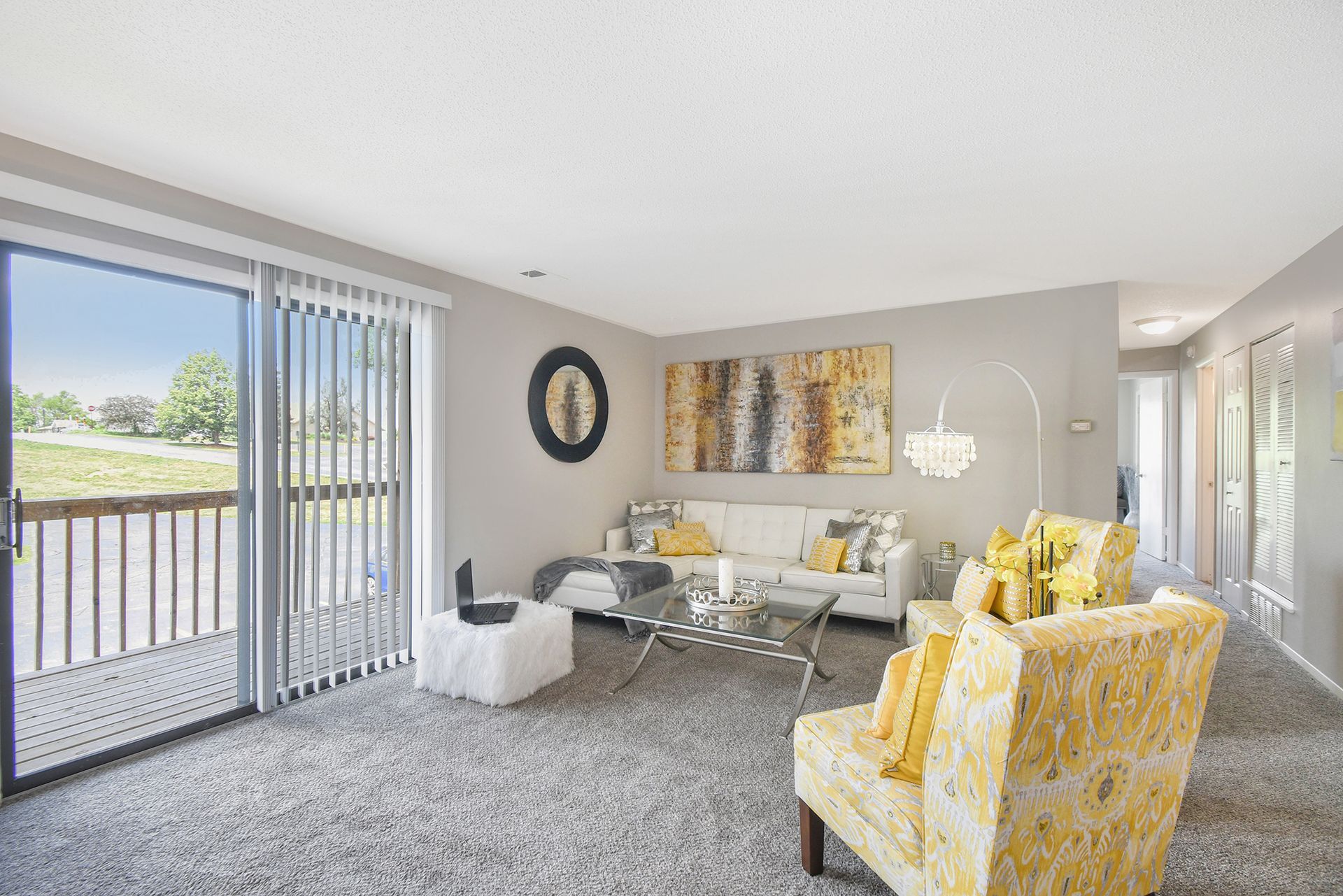 Living room with sliding glass door, white sofa, yellow armchairs, and abstract art.