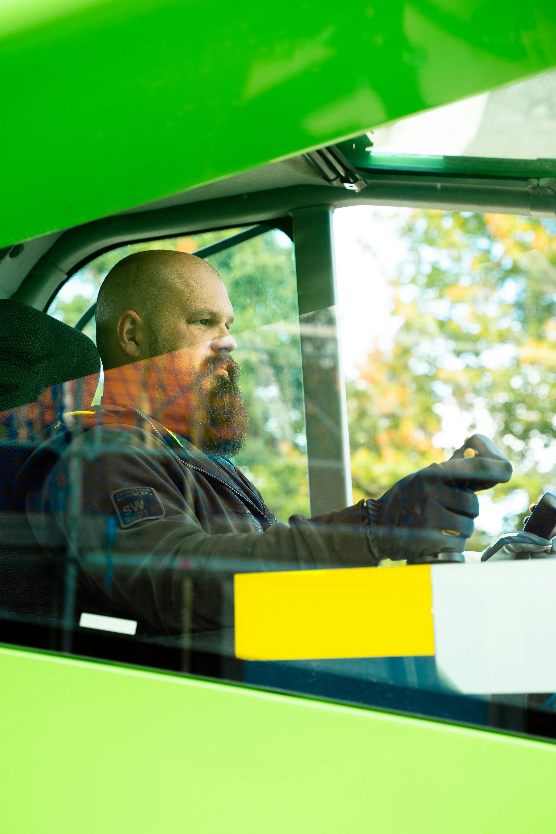 Driver seated in a green vehicle, looking ahead and holding the steering wheel
