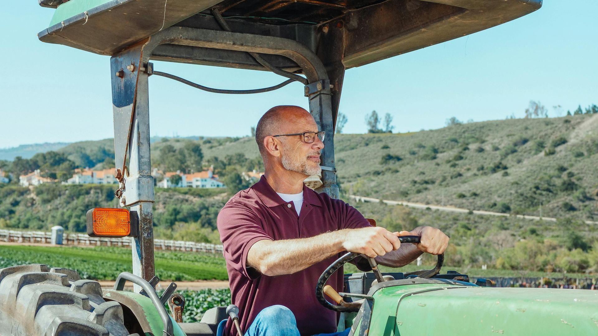 Man driving a green tractor in a sunny rural hillside field