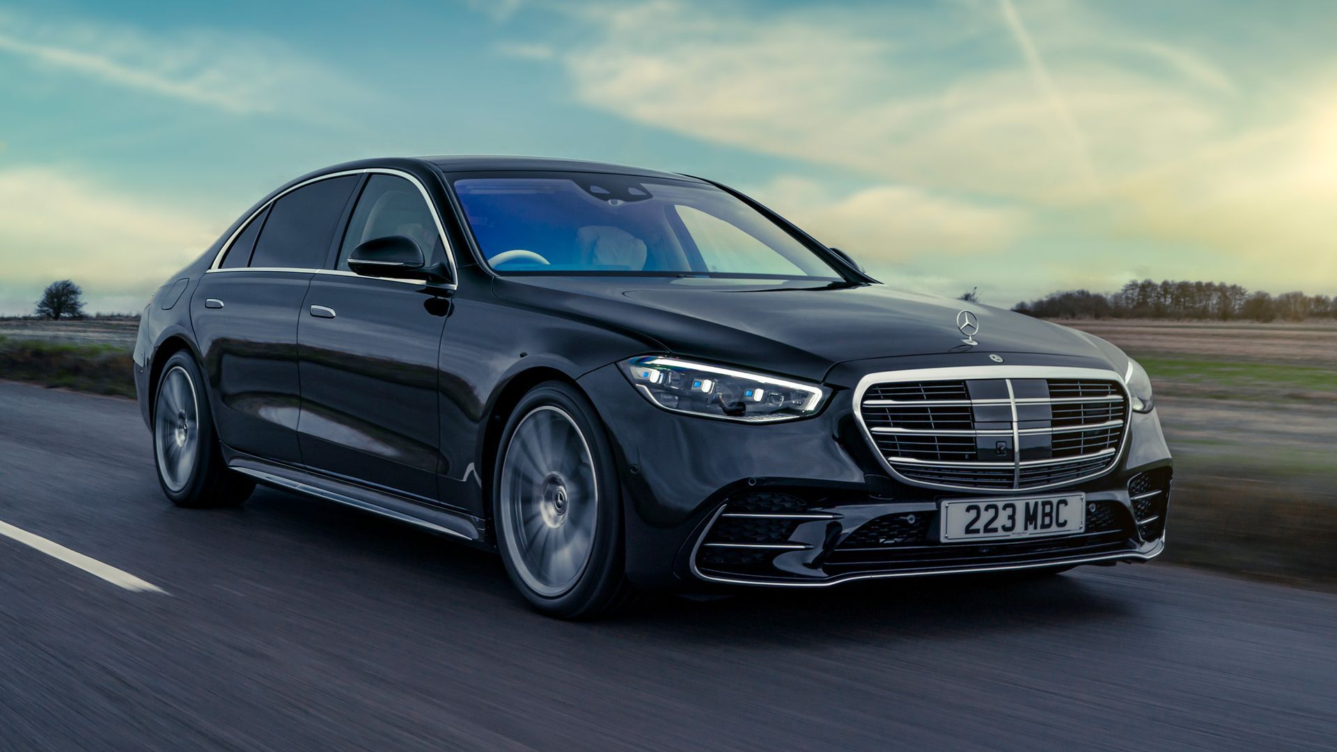 A black Mercedes-Benz S-Class sedan driving on a highway during a bright, sunny day.
