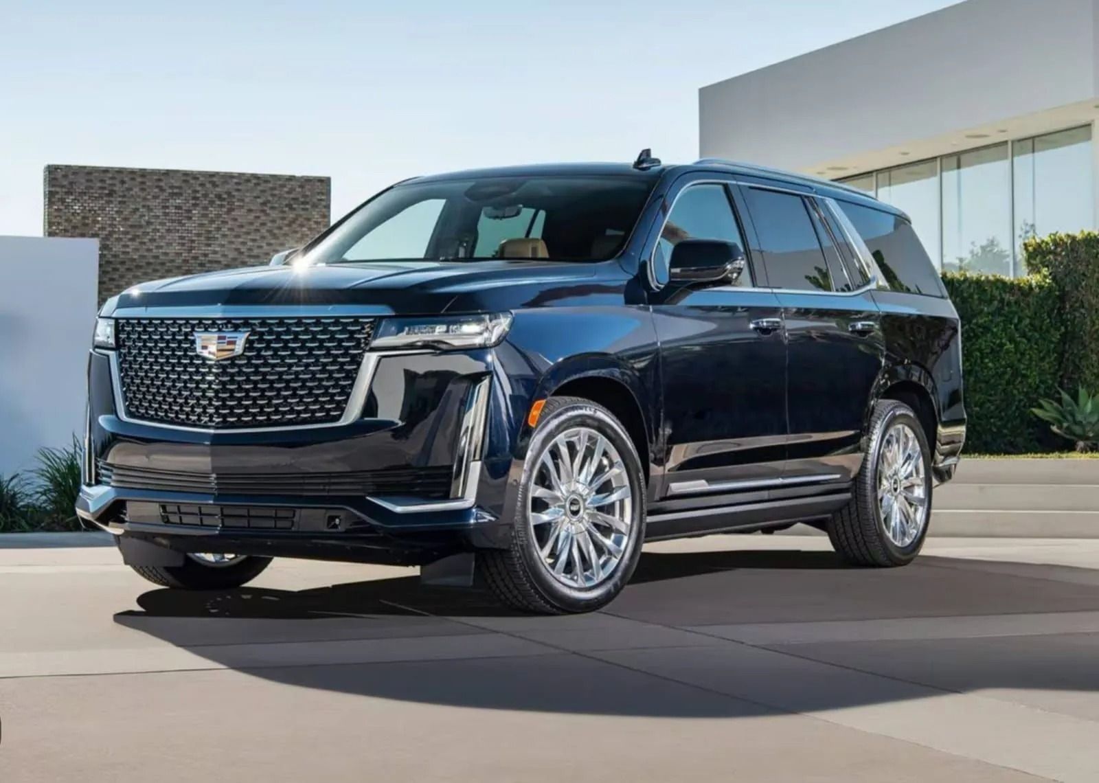 A dark blue Cadillac Escalade parked outdoors on a paved surface in front of a modern building.