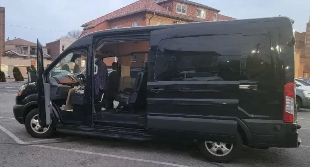 A black passenger van parked in a lot with its side door and front passenger door open, revealing the interior seats.