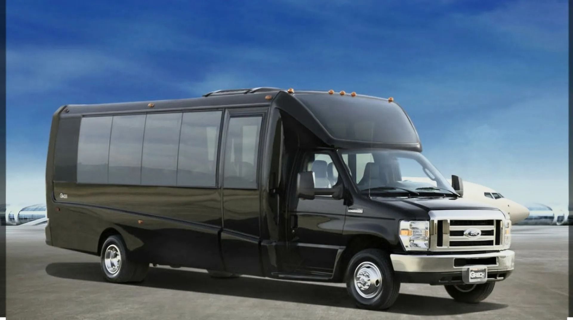 A black passenger shuttle bus parked on an airport tarmac with a faint aircraft in the background.