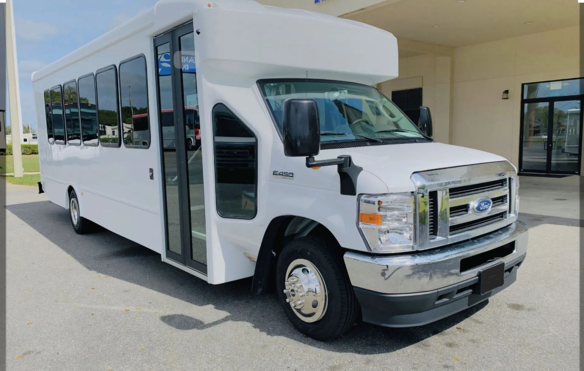 A white Ford shuttle bus parked in a paved lot in front of a building.