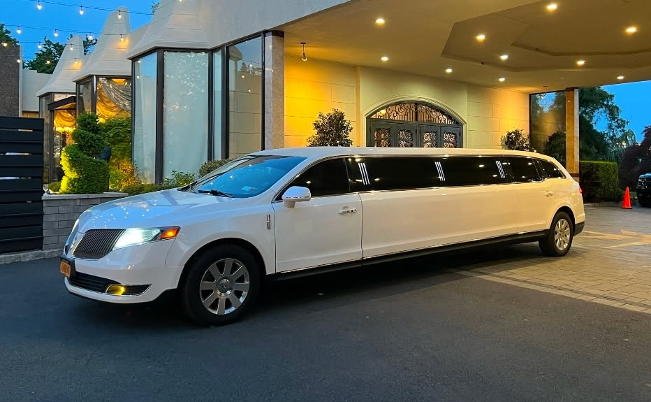 White stretch limousine parked at a hotel entrance under warm lights at dusk