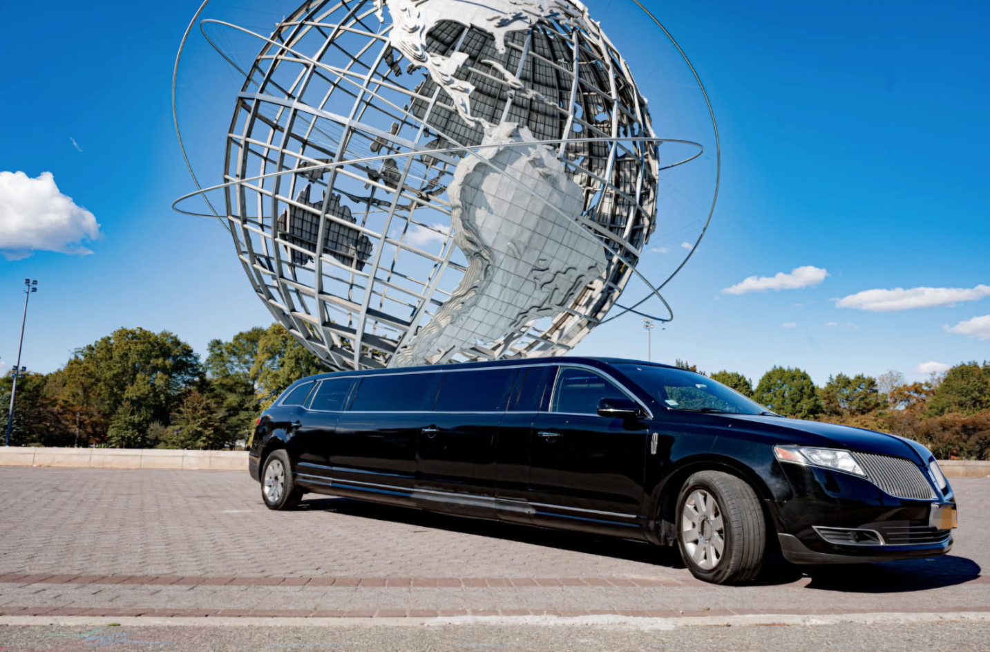 Black limousine in front of a large globe sculpture under a blue sky