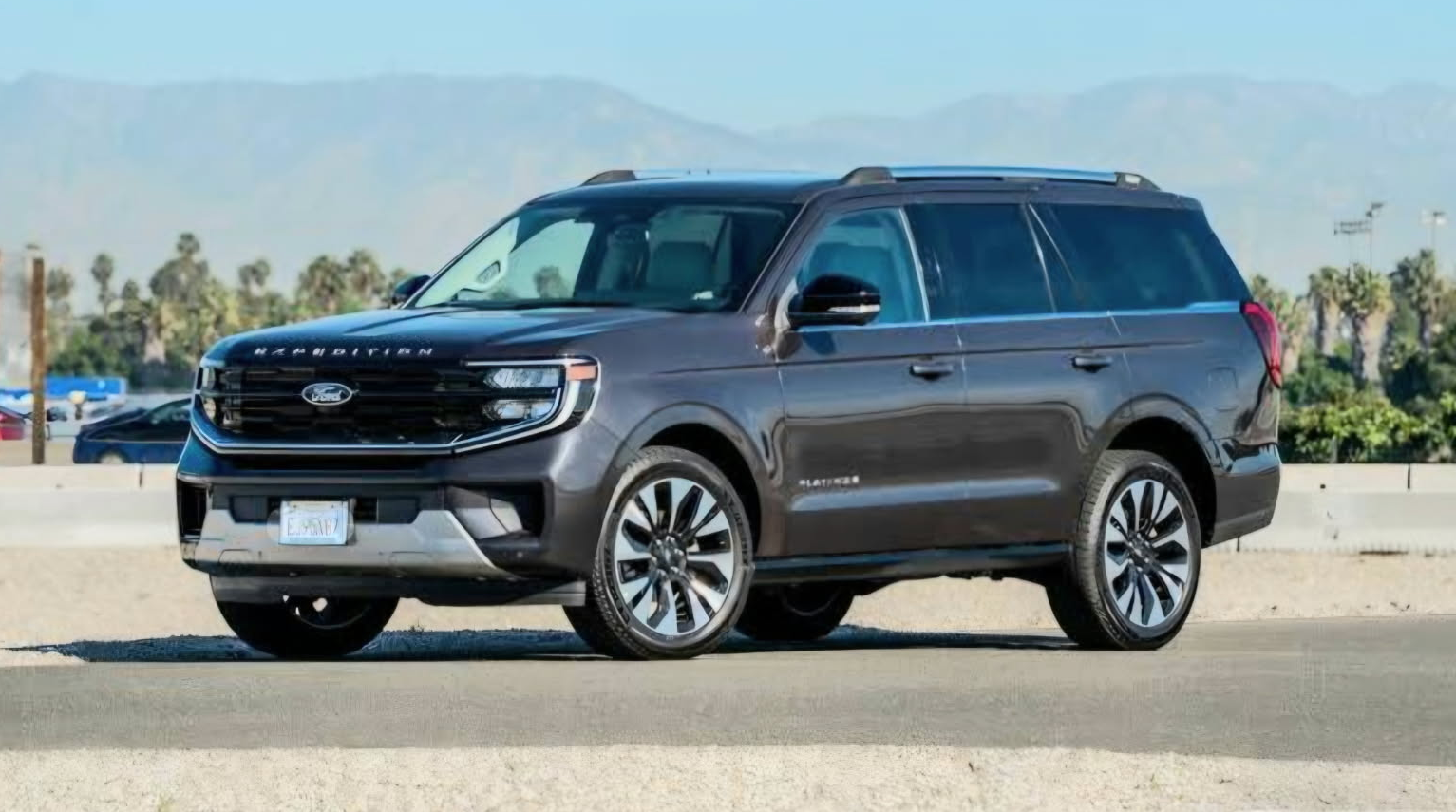 A dark Jeep SUV with black wheels parked in a dry, grassy field on a clear day.