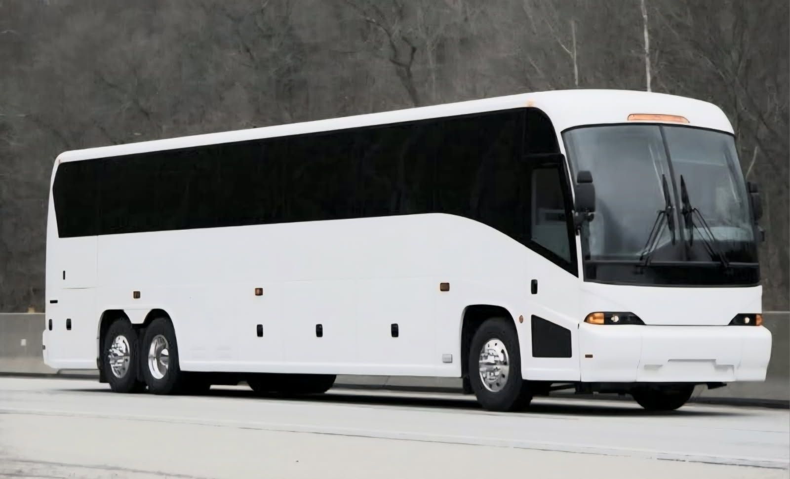 A plain white charter bus driving on a highway with trees in the background.