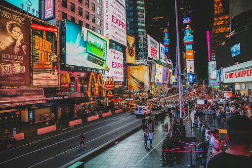 A high-angle view of a busy Times Square at night with glowing billboards, bright city lights, and crowds of pedestrians.