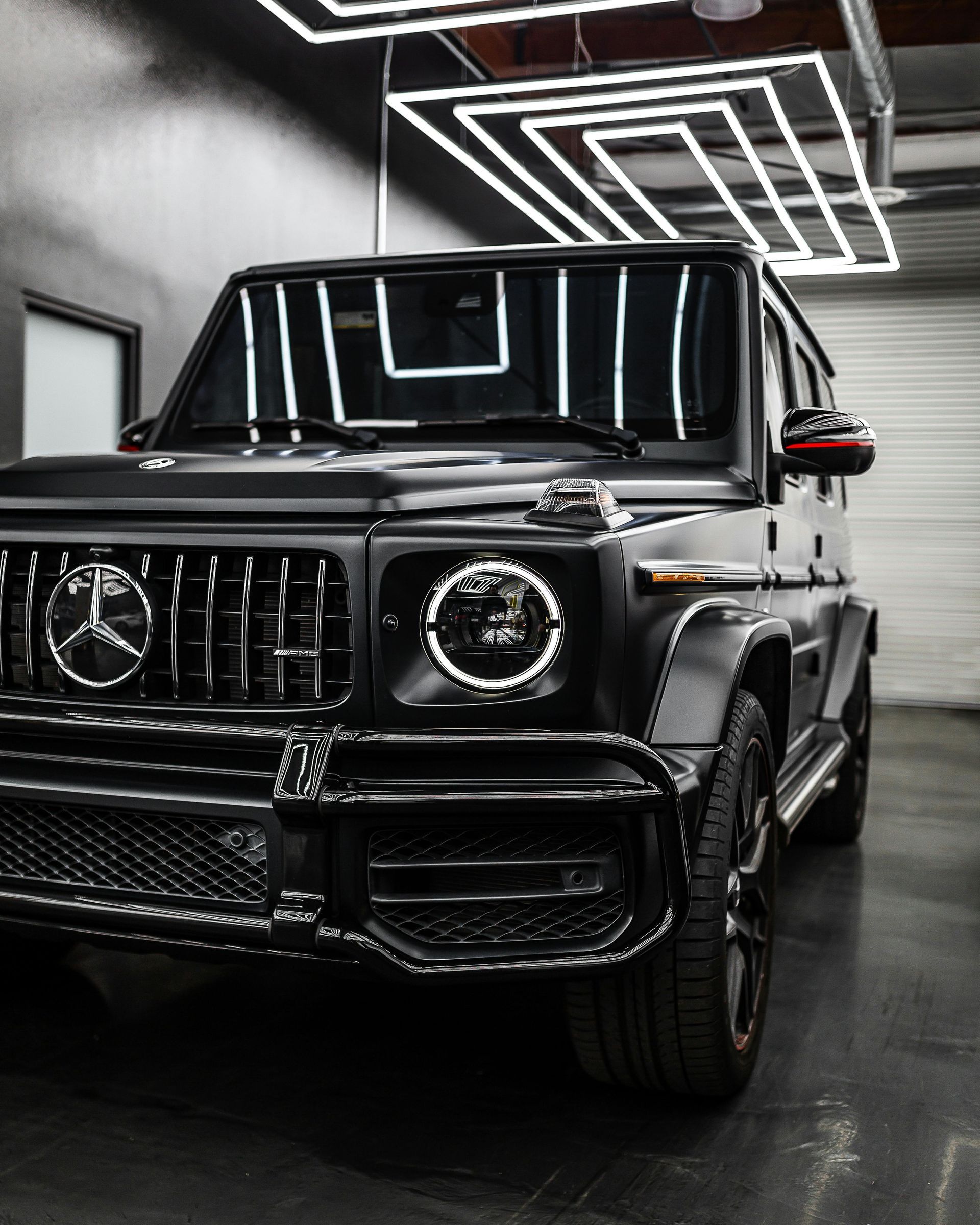 A black Mercedes-Benz G-Wagon parked inside a garage with geometric overhead lighting.