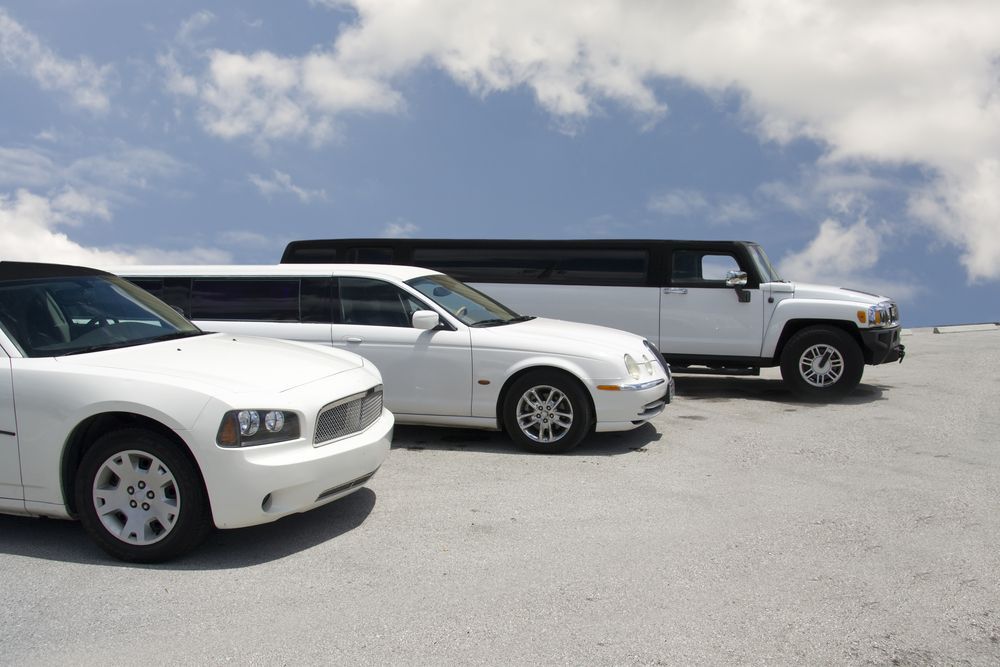 Three white stretch limousines parked in a row against a cloudy blue sky.