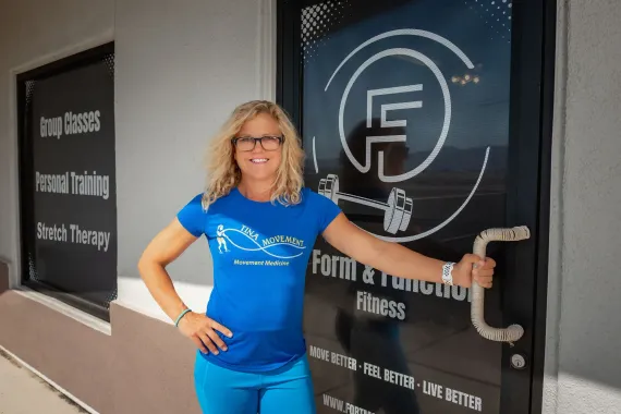 Woman in blue standing by a glass door with a large circular F logo and signage.