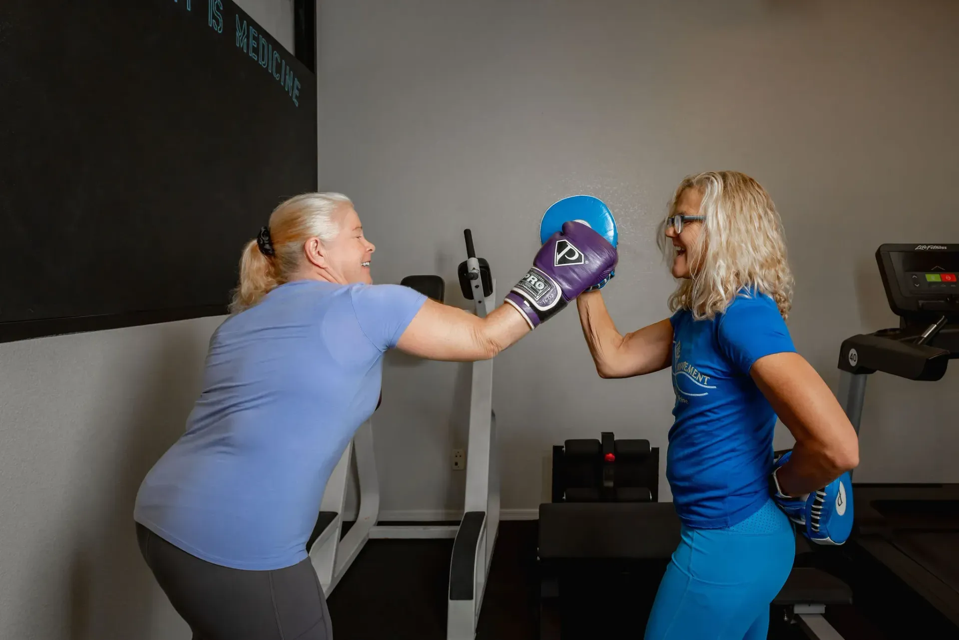 Two women in Form and Function Fitness gym in Fort Mohave, AZ doing a pad-hitting workout, one striking a purple target mitt.