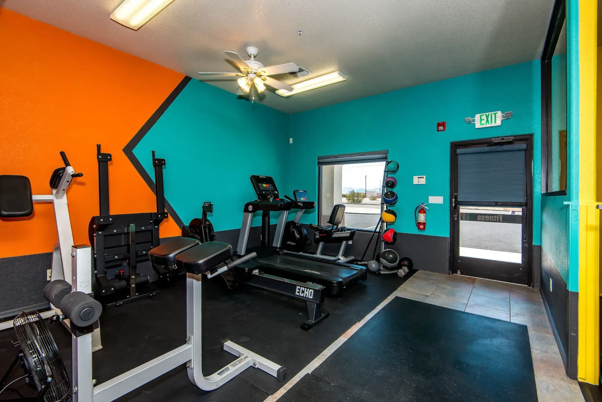 Form and Function Fitness gym in Fort Mohave, AZ with turquoise and orange walls, featuring weight machines, mats, and an open doorway.