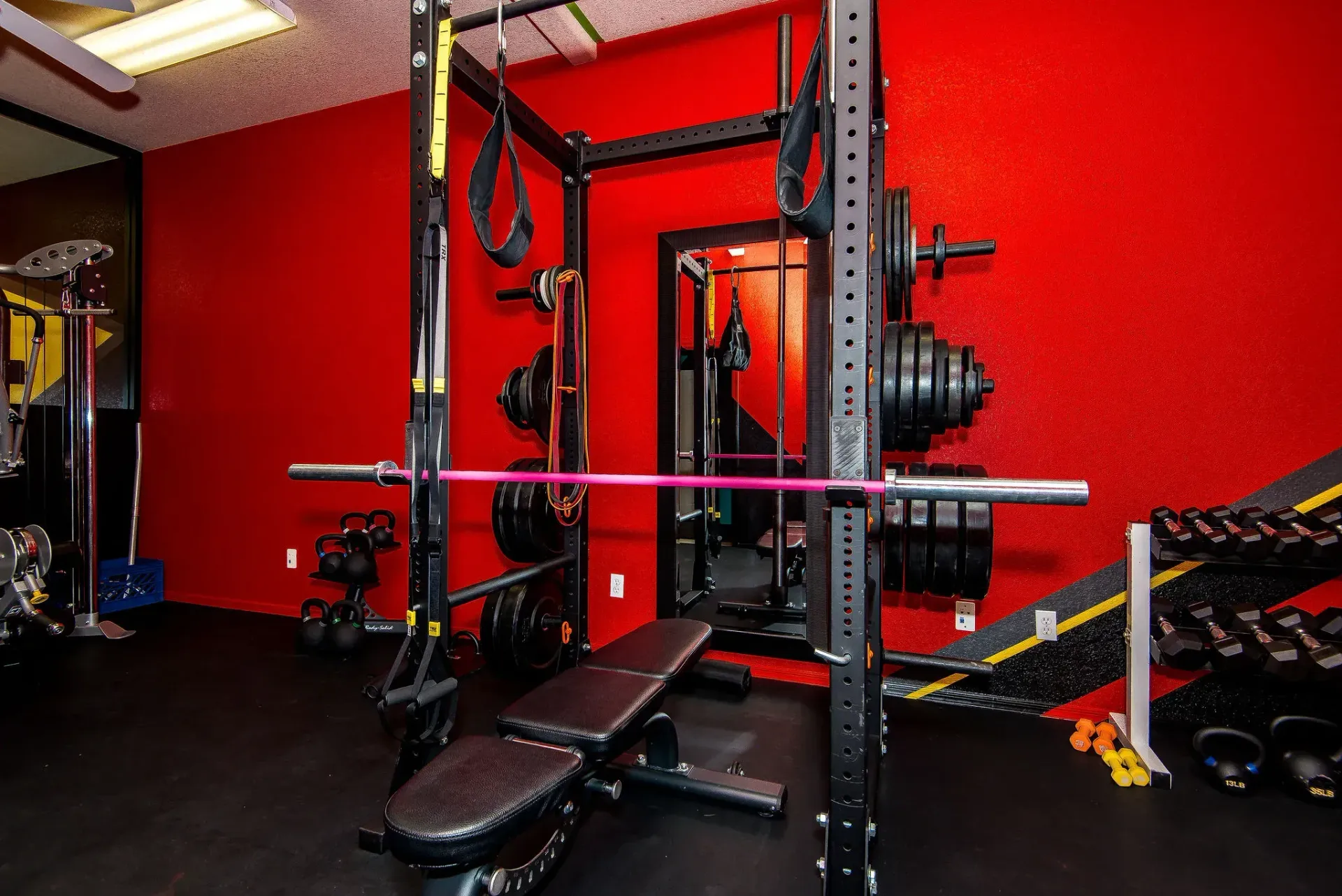 Red Form and Function Fitness gym in Fort Mohave, AZ, with weight bench, squat rack, barbell plates, and cable machine.