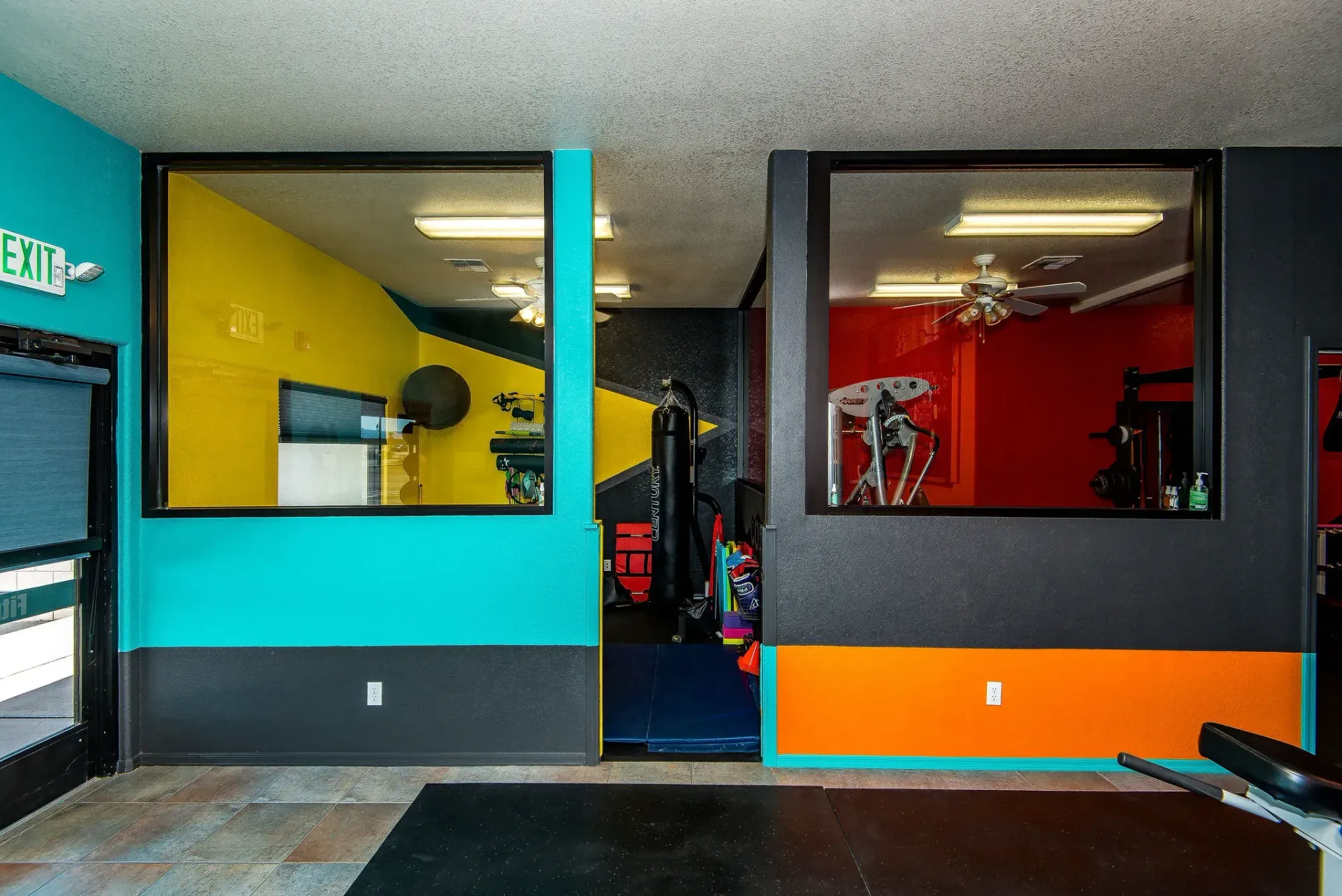 Colorful gym interior with teal, yellow, and red walls and workout equipment visible through glass windows