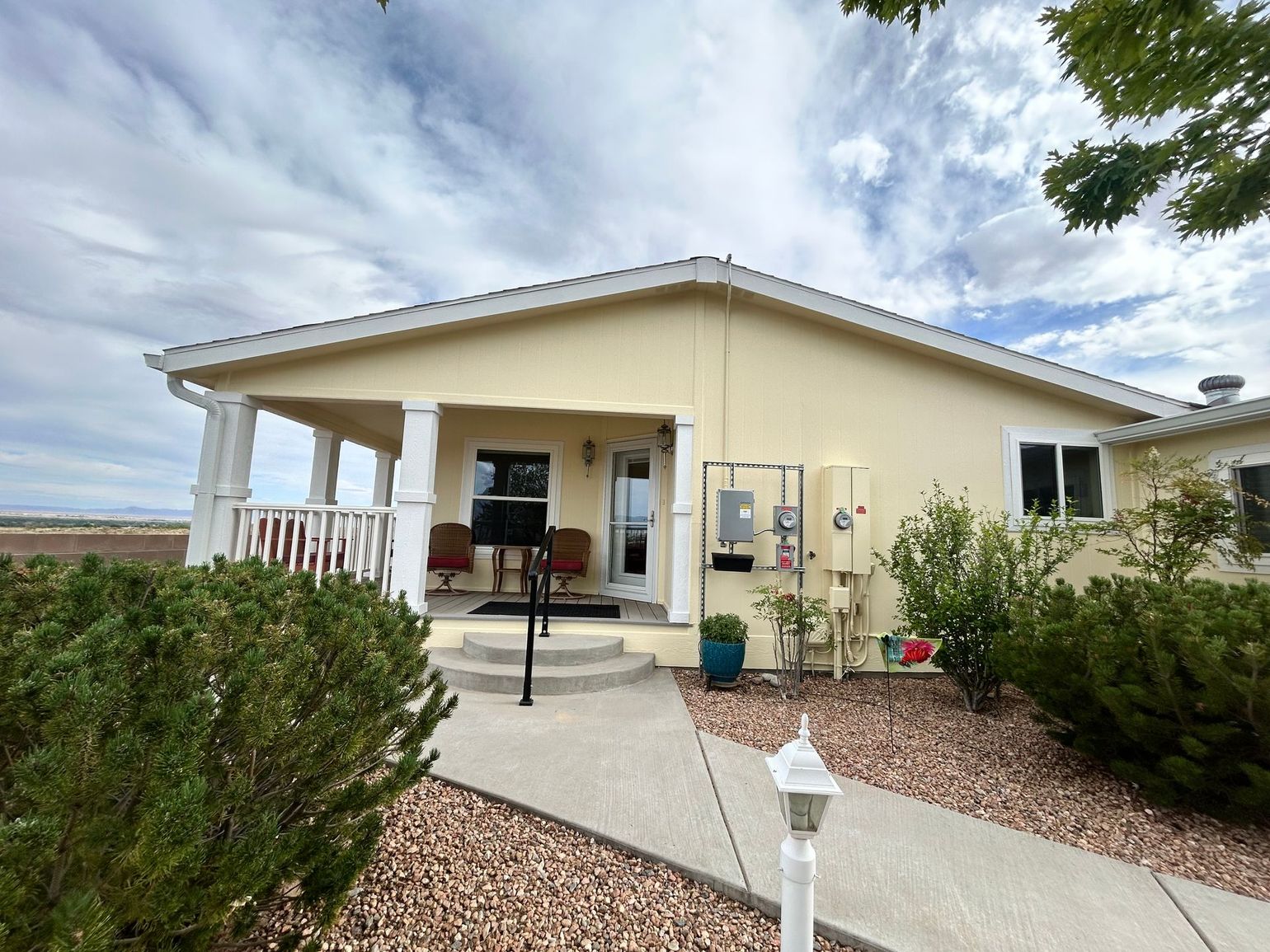 Single-story beige house with a covered porch and desert landscaping under a cloudy sky