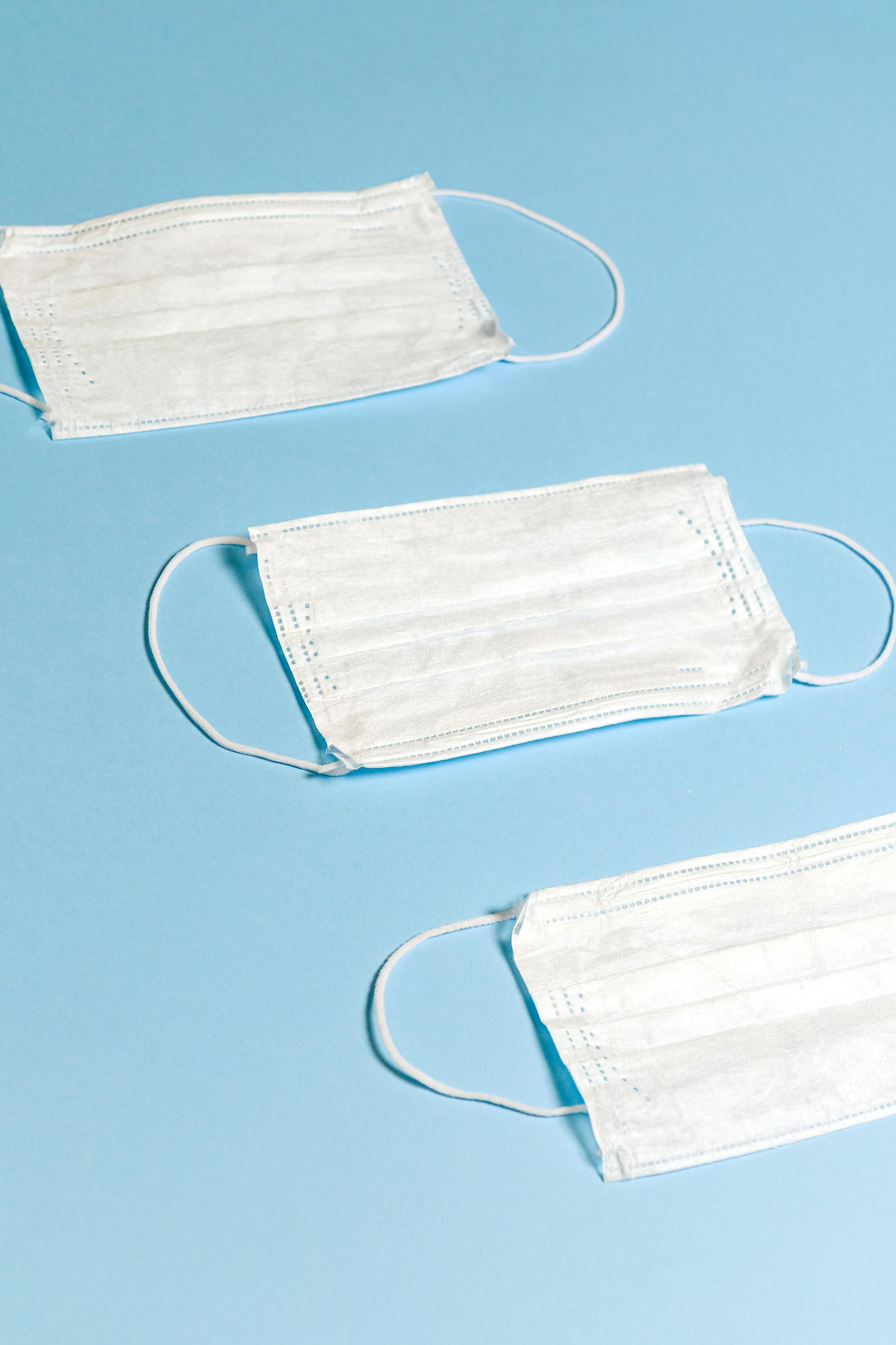 Three white face masks on a light blue background.