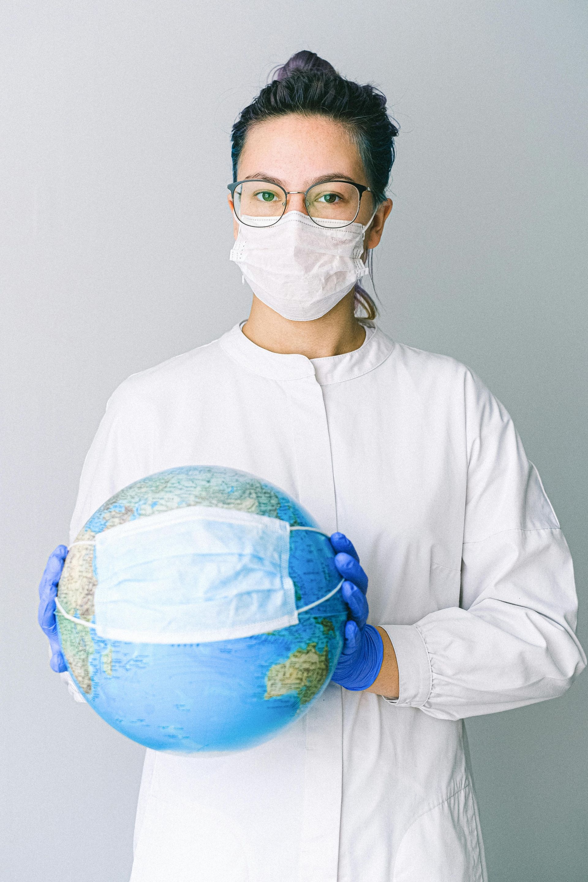 Person in medical gear holding a globe with a mask.