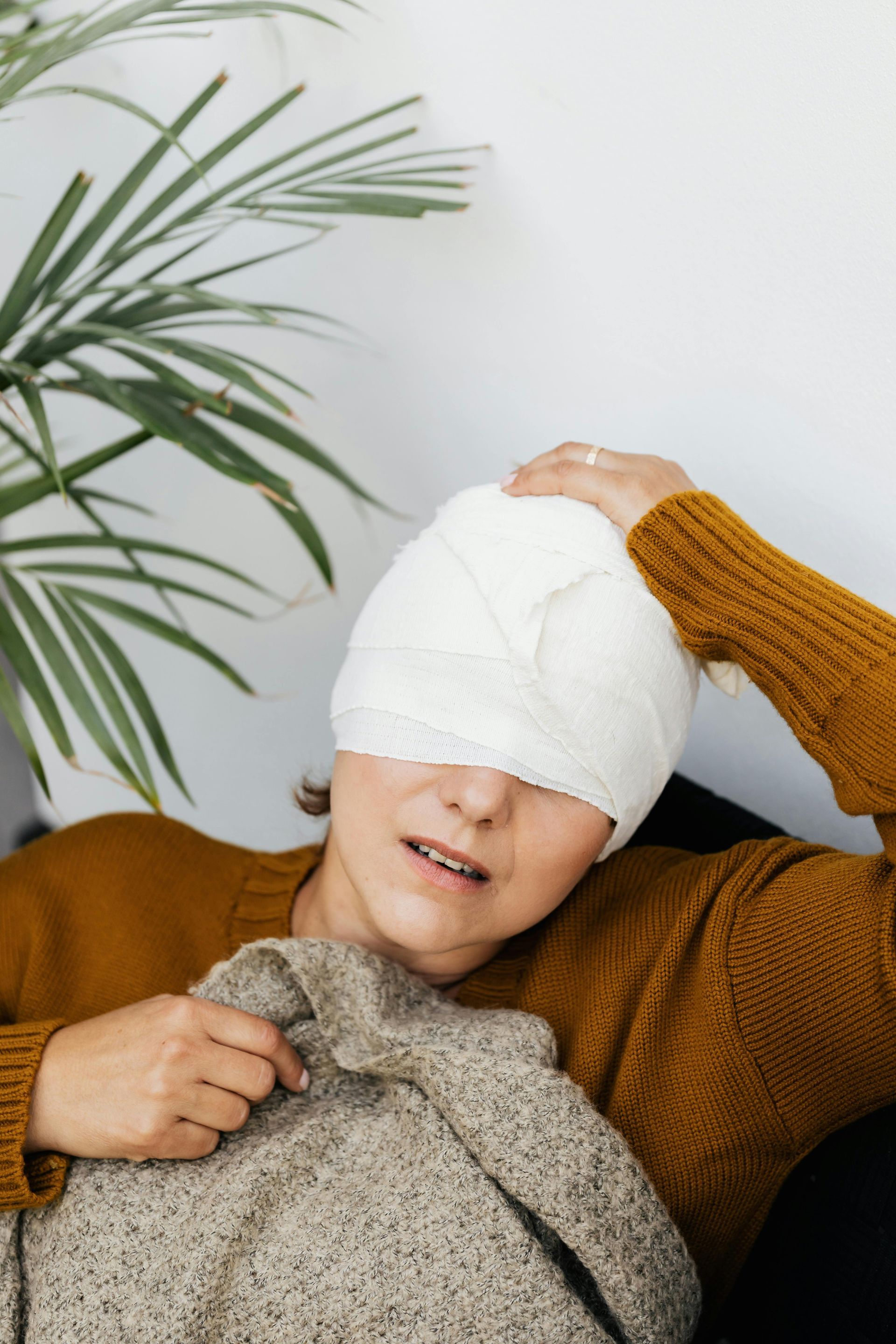 Woman with head wrapped in bandage, appears to be in pain, sitting indoors.