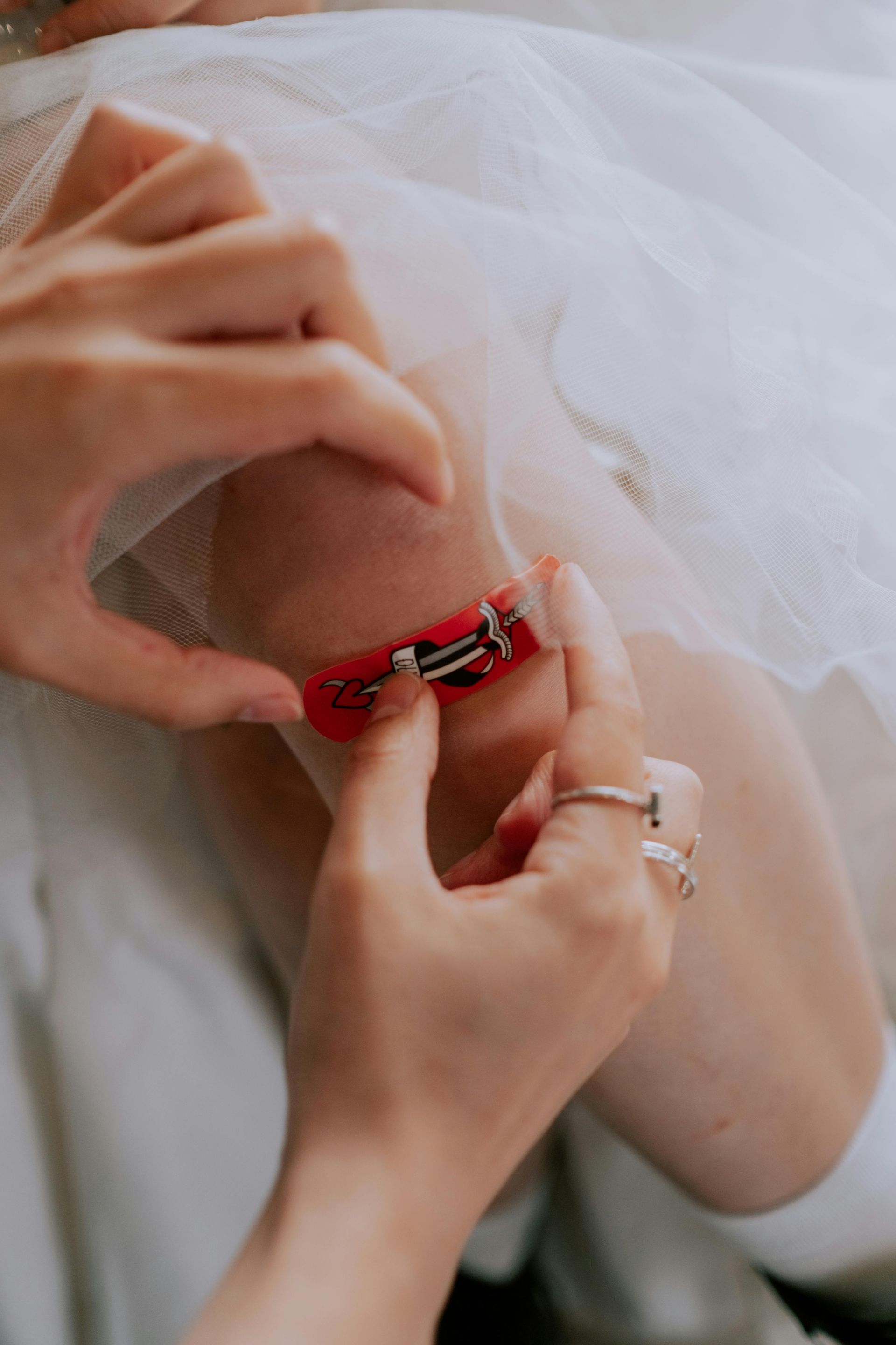 Hands pinning a red and silver embellishment to white fabric.