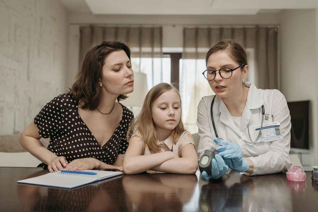 Doctor showing a child and mother a medical device, sitting at a table.